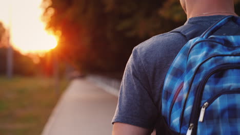 a teenager with a backpack is walking along the road to school only his shoulder and part of the bac