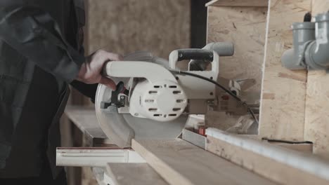 in the woodworking workshop. a worker cuts a board with a miter saw