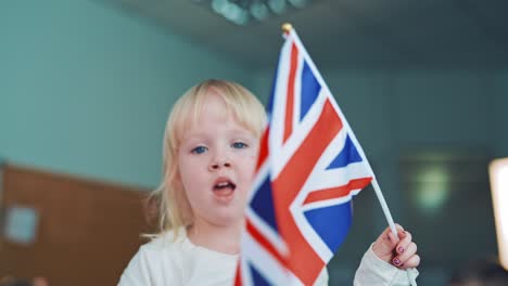 little girl plays with british flag. pretty young child with blond hair holds the flag of great britain. blue,red and white color of the english flag in girl's hands.