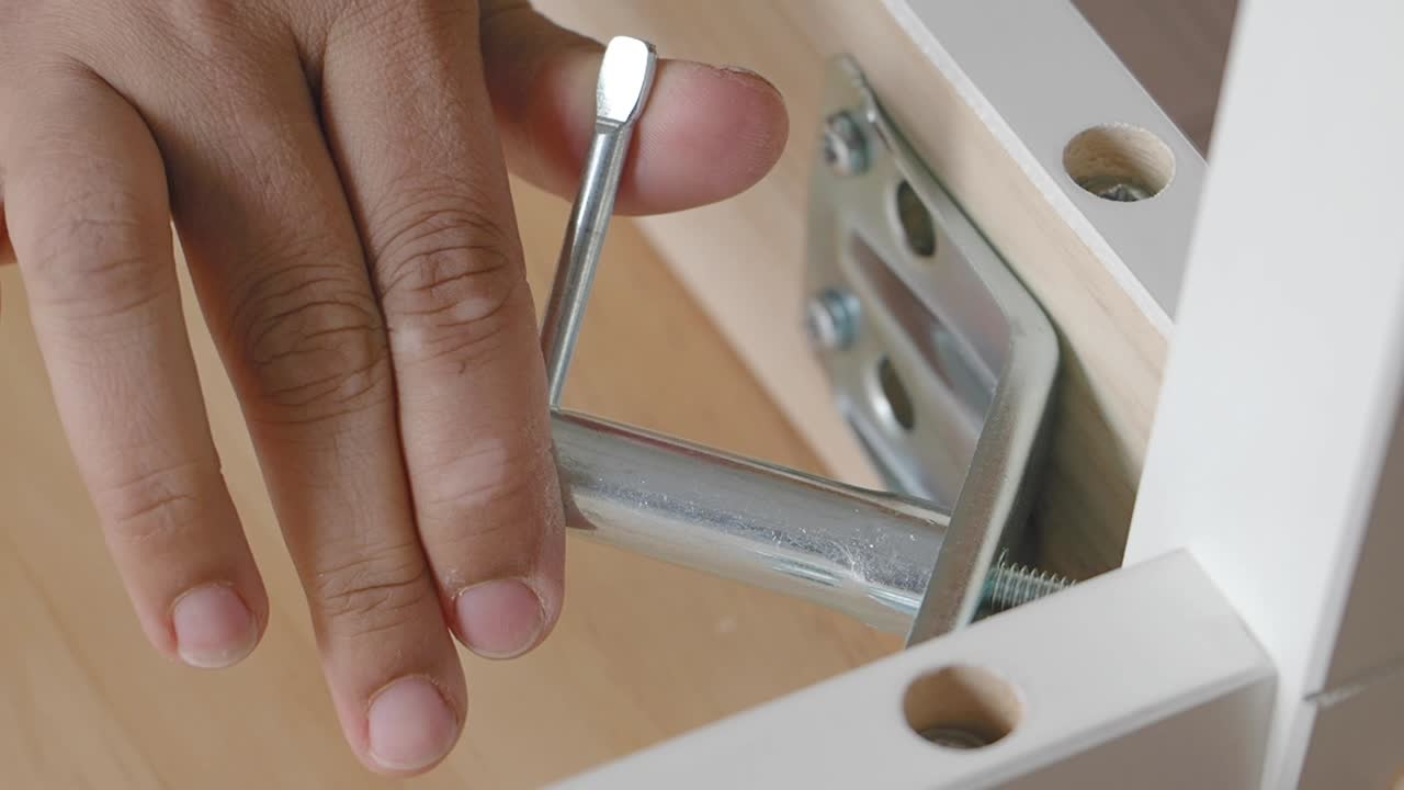 Hand assembling white furniture with a metal bolt
