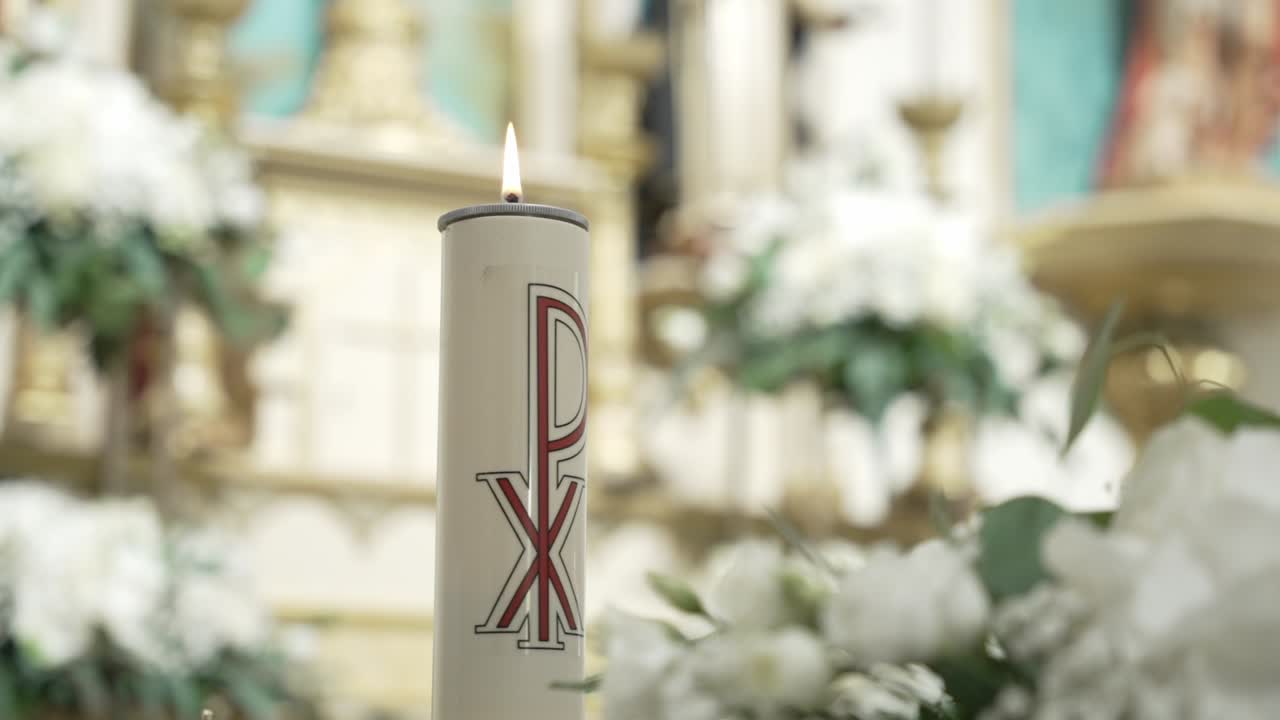 baptismal candle burning inside church with floral decor and blurred altar in background
