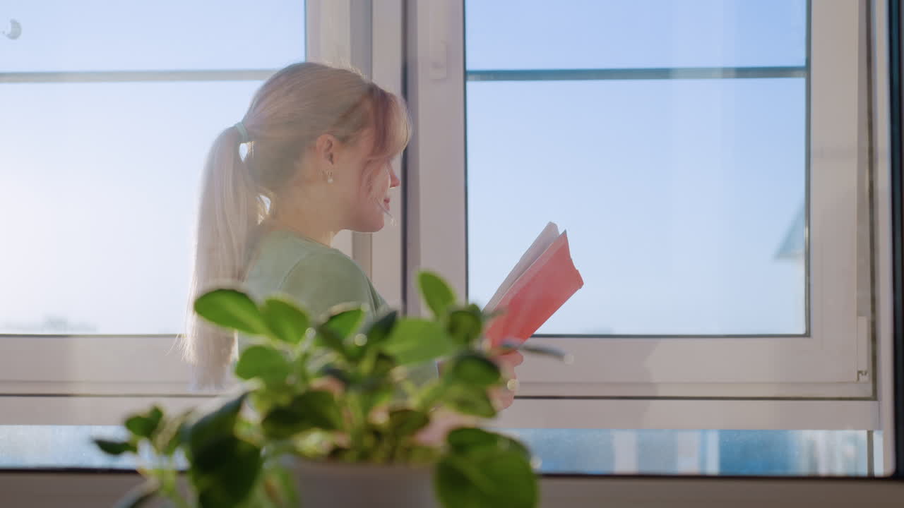 Side view woman standing near window reading book under bright sunlight, enjoying calm moment with natural daylight streaming in, symbolizing relaxation and learning