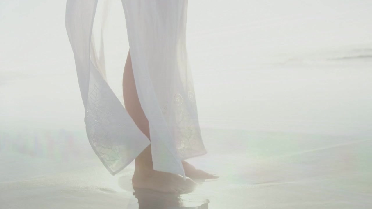 Donna di mezza età che cammina sulla sabbia bagnata, causando un bagliore di luce che accentua lo spacco del vestito per la moda
