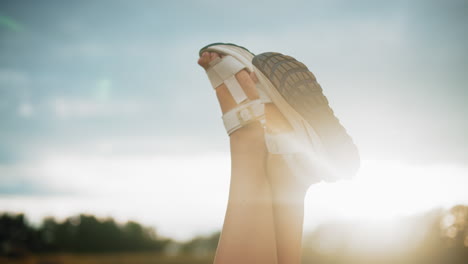 close-up of legs wearing white sandals raised against warm sunlight glow, soft blur background features trees in the distance, creating a relaxing, peaceful outdoor setting