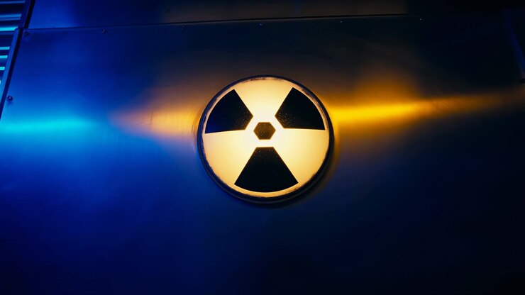 Circular black and yellow radiation emblem remains fixed on brushed metal panel while slow lateral movement exposes cool blue framework and contrasting amber light across wall.