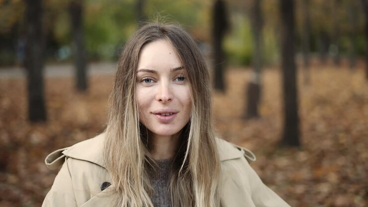 Ritratto di una donna bionda che beve un caffè da asporto nel parco autunnale dorato.