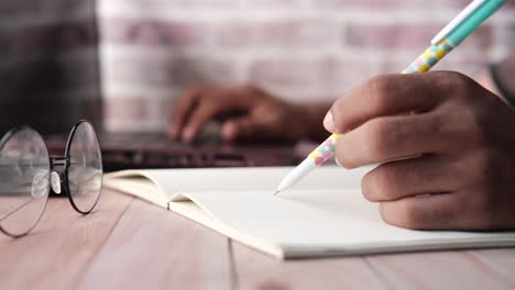 persona escribiendo en un cuaderno en un escritorio con una computadora portátil