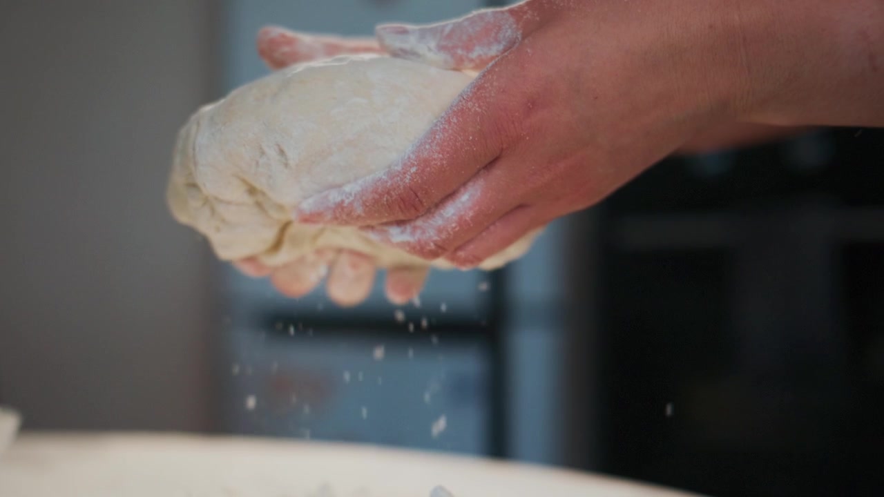 Primo piano di mani che tengono l'impasto con farina che cade al rallentatore.