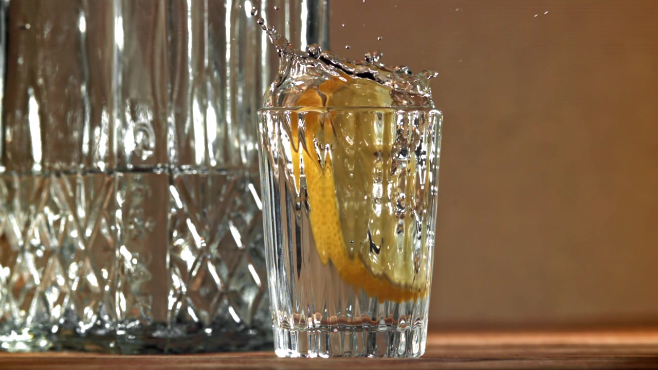 Fetta di limone che cade in un bicchiere d'acqua al rallentatore