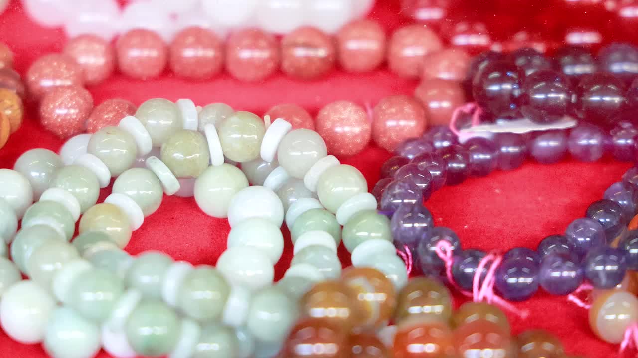 Vibrant beaded bracelets arranged on a red cloth in a Phuket market. Bright lighting highlights the diverse colors and textures