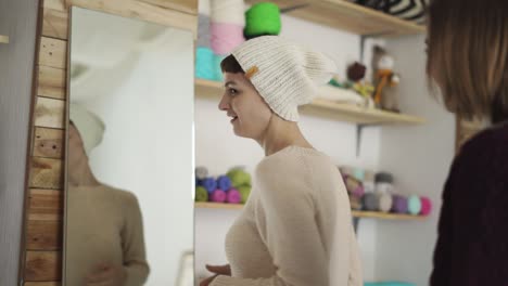 happy woman fitting knitted headdress front mirror in textile workshop