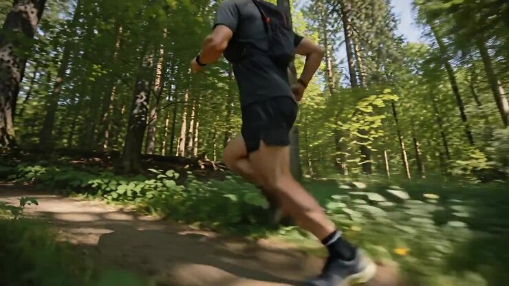 Pushing off, male runner moving along woodland trail, wearing athletic shorts and pack