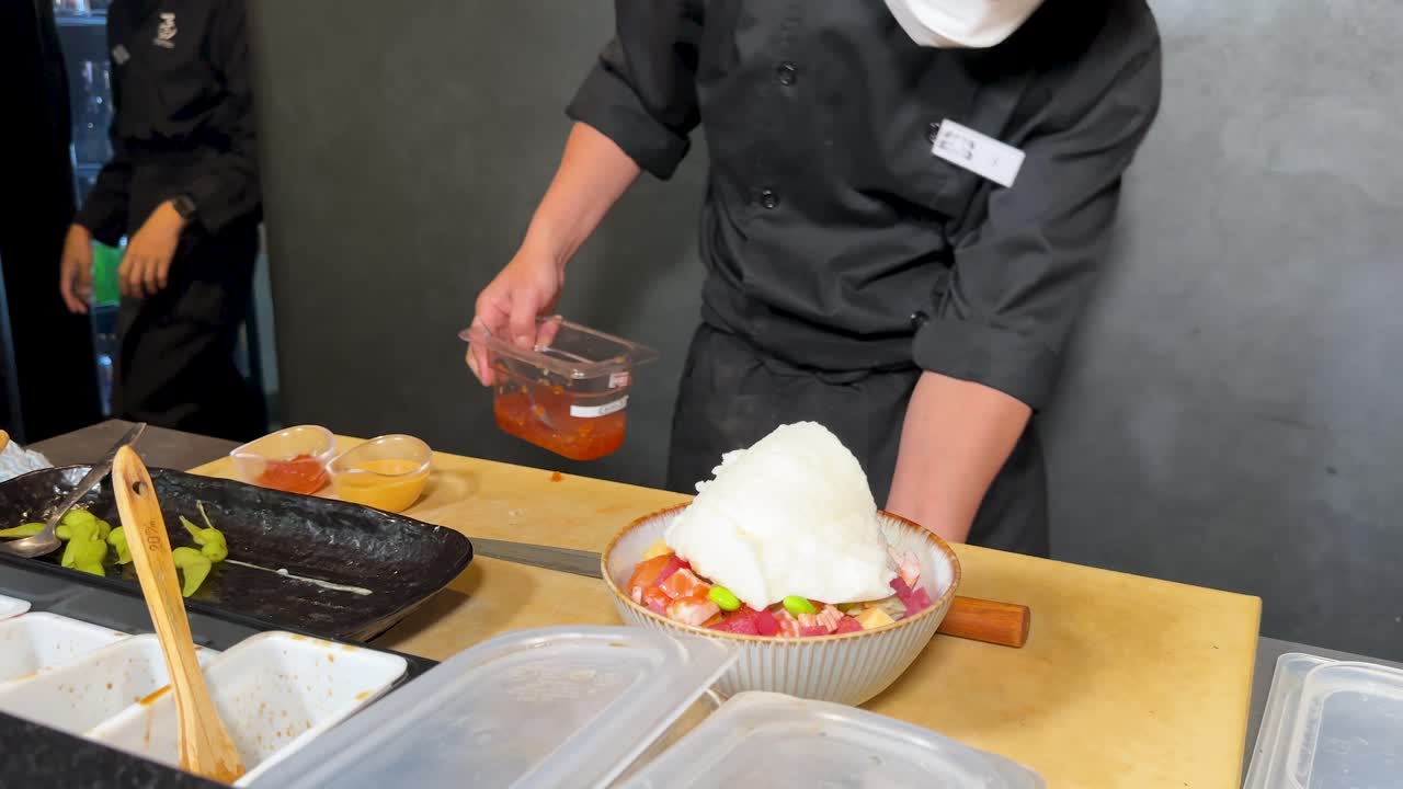 プロの料理人が、鮮やかなオレンジ色の魚卵を色とりどりのポキボウルに丁寧に添えています。