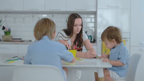 Mom-and-her-two-sons-sitting-at-the-kitchen-table-drawing-colored-pencils-family-drawing-on-the-lawn-in-the-summer.