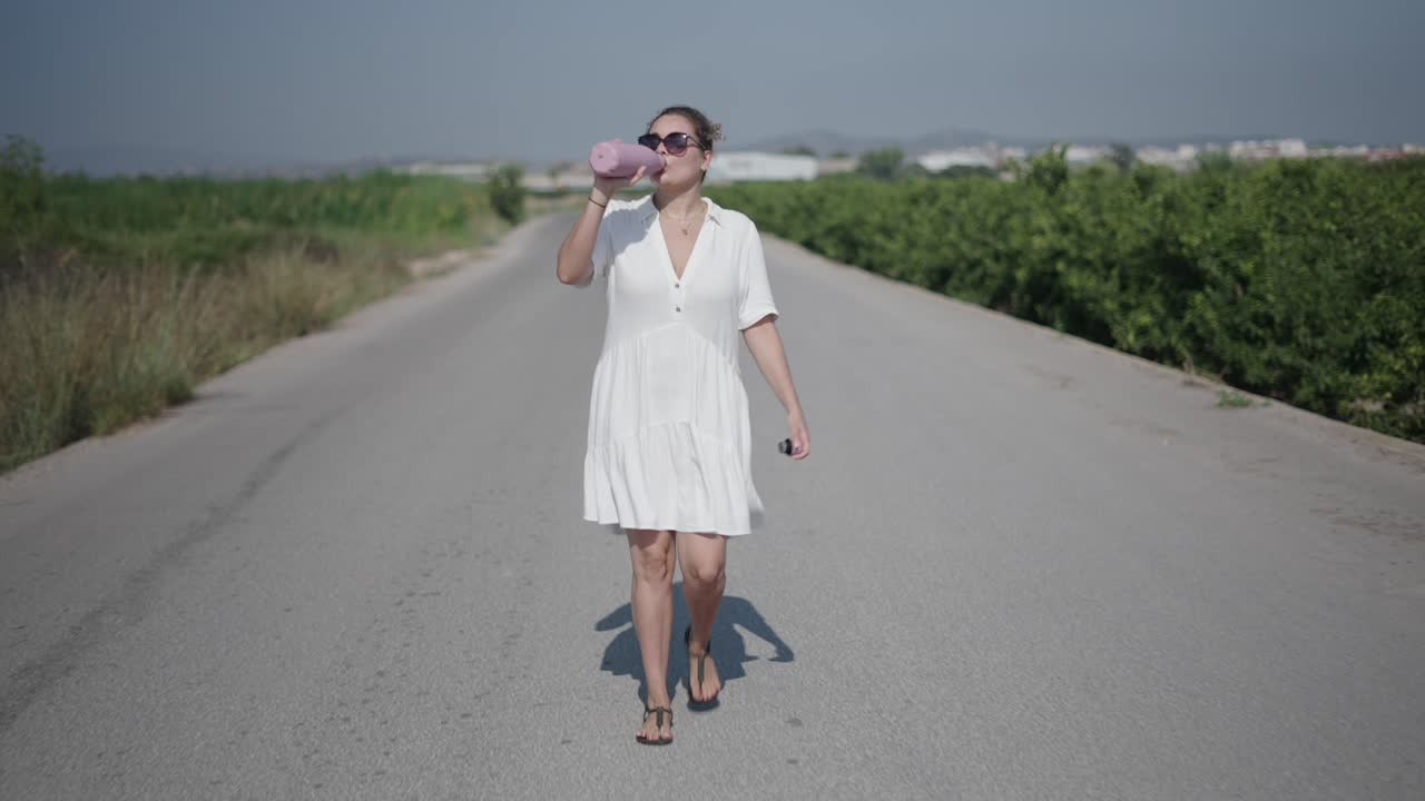 Woman walking on a country road with a pink reusable water bottle