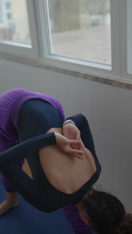 woman practicing yoga backbend posture near a window