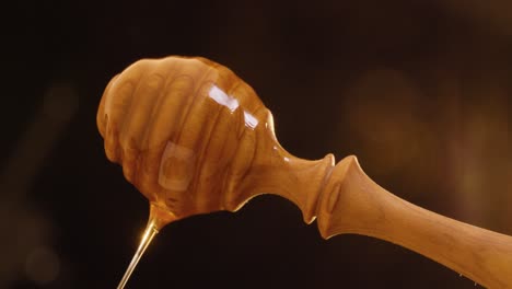 static shot of rotating honey spoon with delicious dripping honey against black background