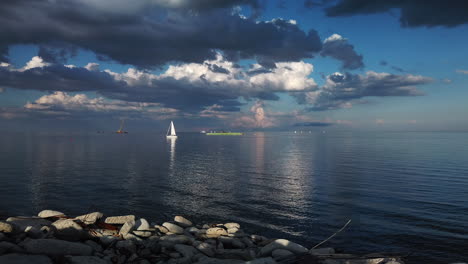 wide shot of stunning lake vista on a calm day, with passing sailboat and reflections on water