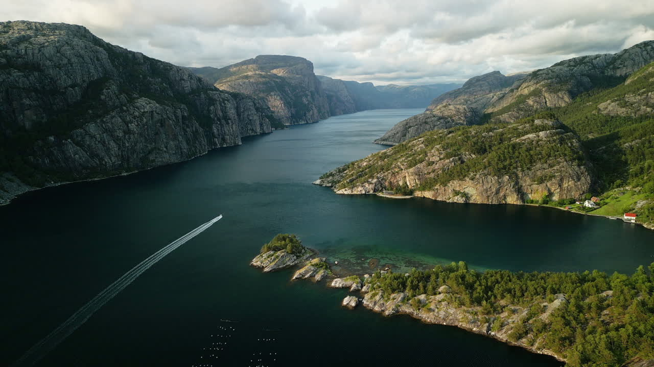 Drohnenaufnahme am Abend vom Lysefjord in Richtung Preikestolen während des Sonnenuntergangs. Ein Schnellboot fährt auf dem Wasser. Die tief stehende Sonne scheint in die Szene und erzeugt eine wunderschöne Atmosphäre.