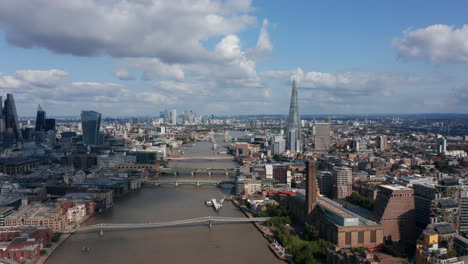 Aerial-panoramic-view-of-large-city.-Forwards-fly-above-River-Thames.-Millennium-Footbridge-leading-to-Tate-Modern-art-gallery.-Modern-skyscrapers-in-background.-London,-UK