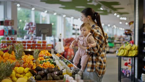 confident brunette girl mother of a small child holds her daughter in her arms and examines the goods on the counter in a supermarket