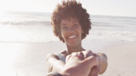 retrato de una mujer afroamericana sonriente de la mano en una playa soleada