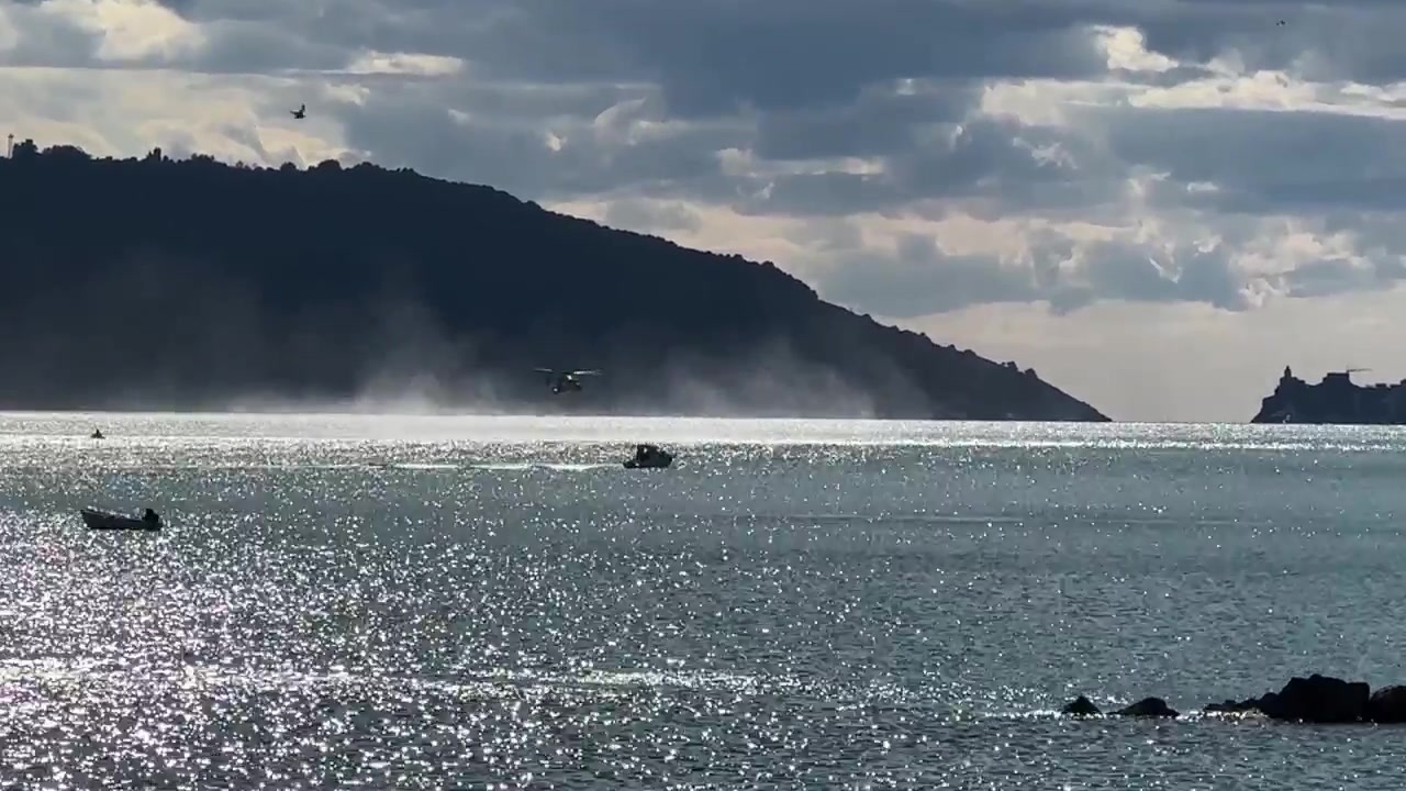 ラ・スペツィア湾上空での海上演習中、低空でホバリングするイタリア海軍のヘリコプター。きらめく海、沿岸の丘、そして手前には小型ボートが見える