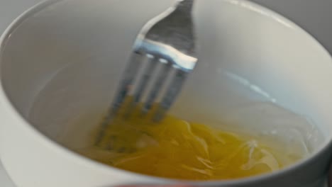 slow-motion close-up of eggs beaten in a white bowl with a fork