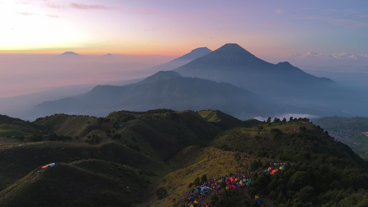 Vista aerea di un campeggio in montagna con un grande gruppo di tende colorate di escursionisti, sullo sfondo di un paesaggio vulcanico mozzafiato e cieli all'alba. Paesaggio del Monte Prau, Indonesia.