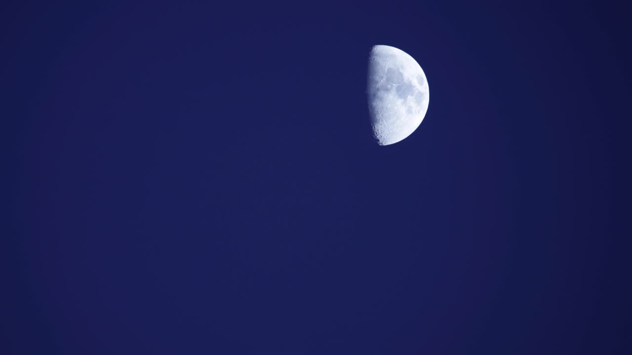 Meia lua (quarto crescente) atravessando o céu azul claro ao entardecer