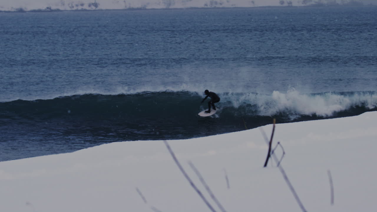Surfer carving Arctic waves near Icelandic coastline under overcast winter skies, slow motion tracking