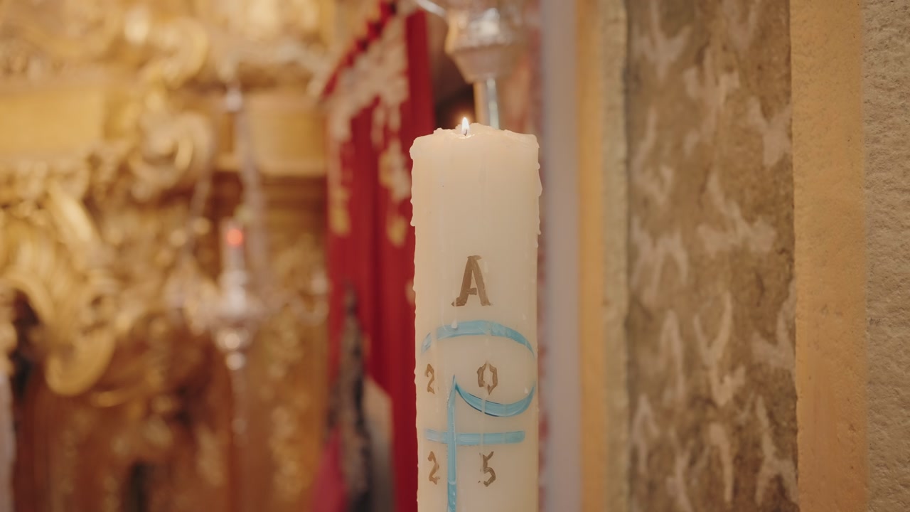 burning paschal candle marked with alpha omega and year inside ornate church