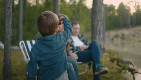 Una-Familia-Con-Dos-Hijos-Pequeños-Descansa-En-La-Naturaleza-El-Fin-De-Semana-De-Verano,-Los-Padres-Y-Los-Niños-Alegres-Disfrutan-Del-Relax-En-La-Orilla-Del-Lago-Del-Bosque.