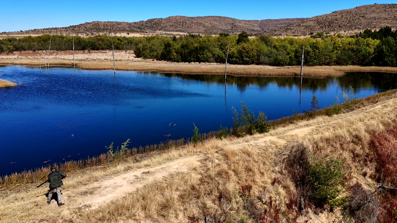 Real time drone view of man clay pigeon shooting over remote farm dam