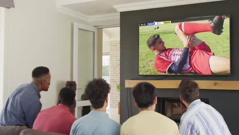 diverse friends supporting and watching tv with diverse male soccer players playing match on screen