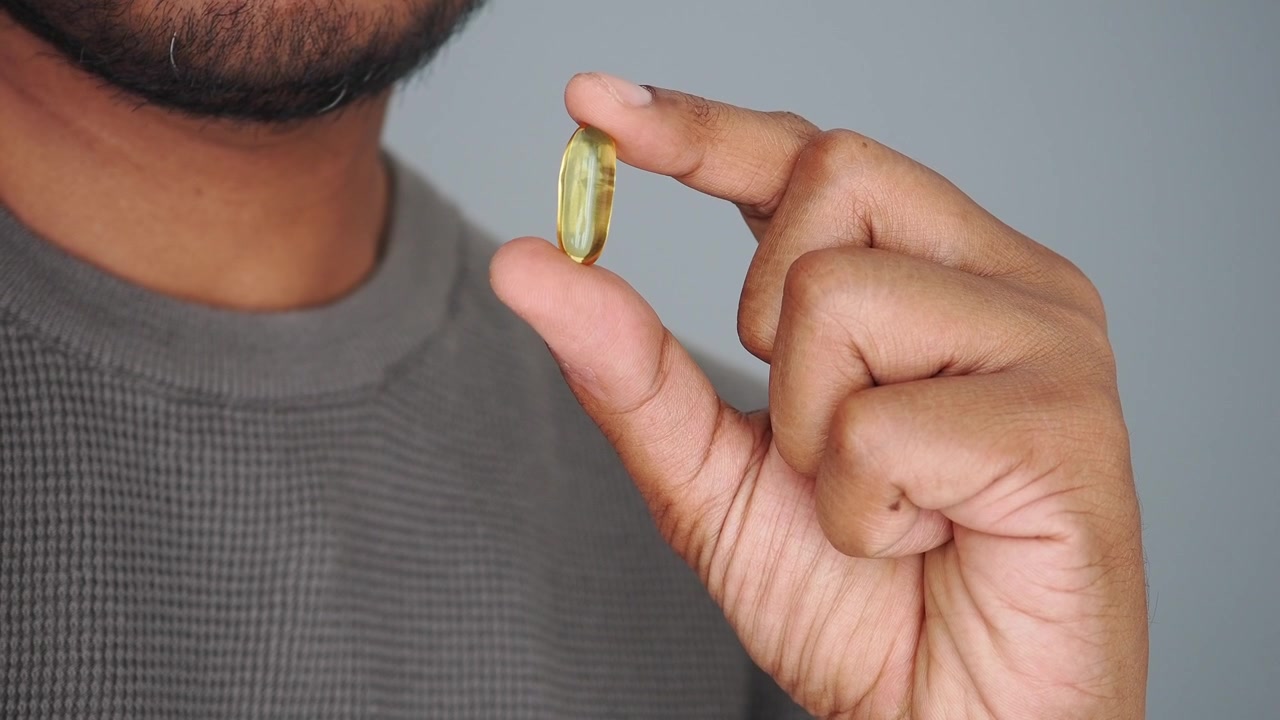 Uomo che tiene una capsula gialla di olio di pesce Omega-3