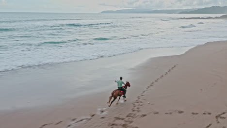 Toma-Aérea-De-Drones-De-Un-Solo-Hombre-Montando-A-Caballo-Galopando-A-Lo-Largo-De-La-Playa-En-Tambor,-Costa-Rica