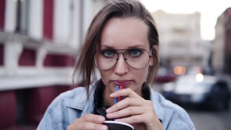 splendida ragazza bionda con un leggero trucco da giorno guardando la telecamera, bevendo una bevanda con una cannuccia e sorridendo. vestita con stile