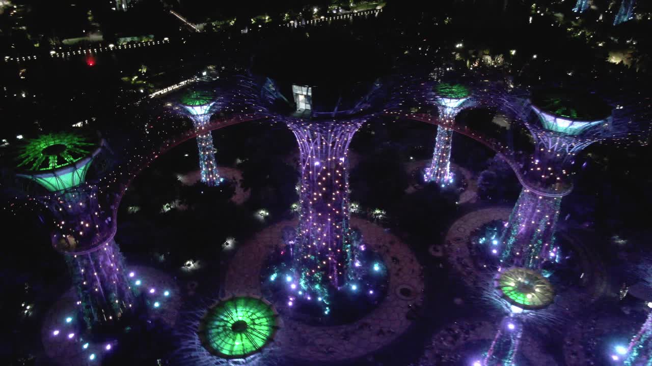 Flying over the illuminated tree structures in the Gardens by the Bay in Singapore at night