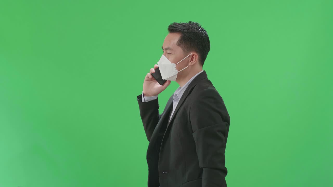 Side View Of Asian Business Man Talking On Mobile Phone While Walking On Green Screen Chroma Key, Wear Medical Mask
