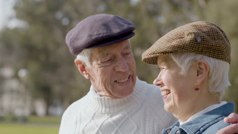 adorable pareja de ancianos besándose y hablando mientras disfrutan juntos del día soleado en el parque