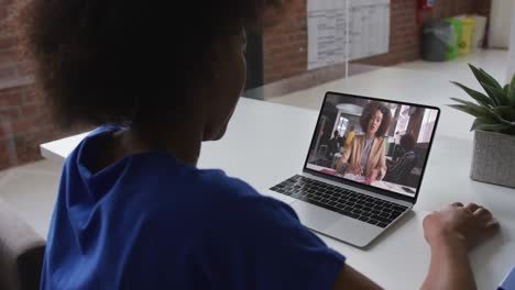 Back-view-of-african-american-woman-having-a-video-call-on-laptop-with-female-colleague-at-office