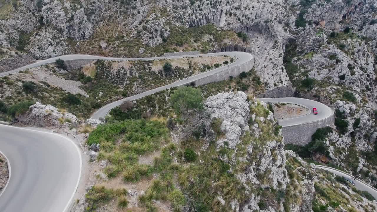 Amazing drone revealing shot in 4k of crazy serpentines in Mallorca with cars driving through and two people downhill skating - Curvy streets in majorca - Serra de Tramuntana - Spain balearic islands
