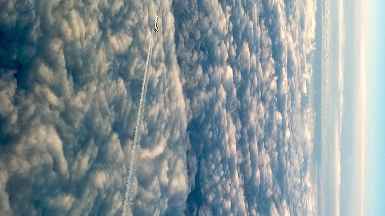 video aéreo de un avión volando por encima de las nubes, dejando un rastro de vapor en el cielo azul