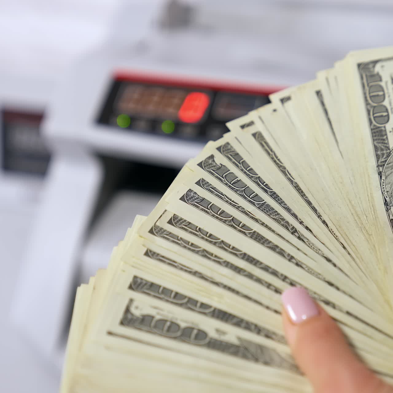 Dollar banknotes in woman's hands. Woman holding a large sum of money on the blur background of electronic counter machine. Close-up. Bank and finance