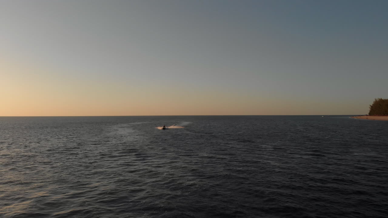 아름다운 일몰 동안 제트 스키를 타고 있는 한 여성이 텅 빈 바다에서 카메라를 지나쳐 속도를 냅니다.
