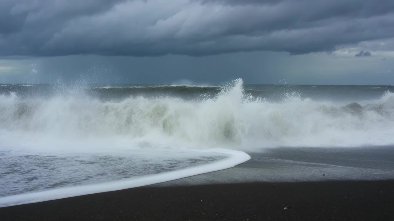 Face à la houle de tempête, des vagues déferlantes s'écrasent sur une plage de sable noir, poussant de l'écume blanche sur le rivage.