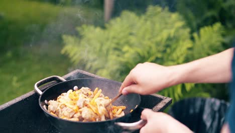 close-up young man makes pilaf in a cauldron on grill on an open fire on birch bark