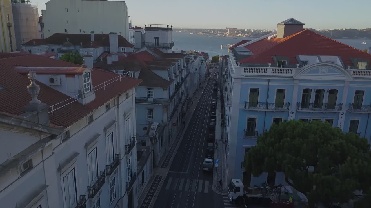 Ripresa aerea in discesa con drone, all'indietro sopra il traffico e la Rua do Alecrim, circondata dalla città di Lisbona, Portogallo, in una serata di sole