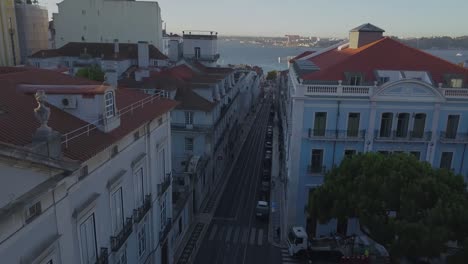 aerial, descending, drone shot, backwards over traffic and the rua do alecrim, surrounded by the city of lisbon, portugal, on a sunny evening